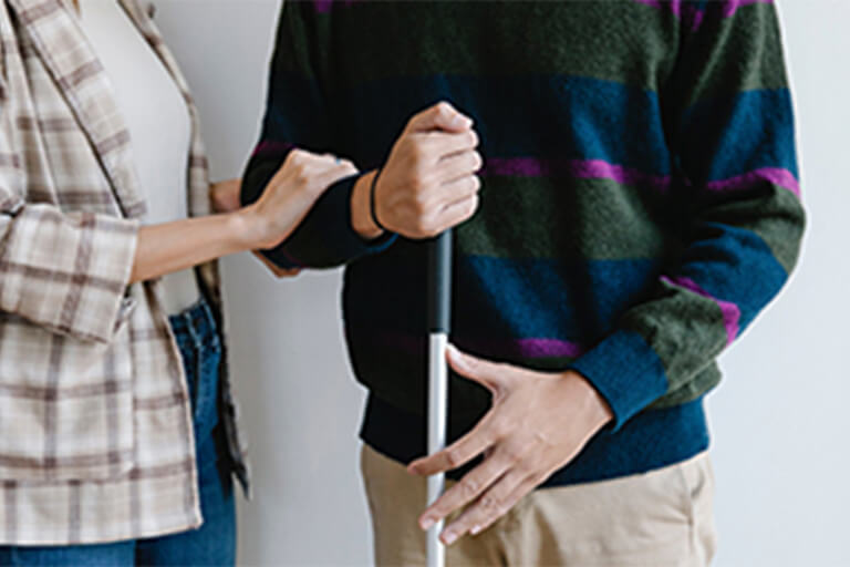 A woman holding onto the arm of another person with a walking cane.