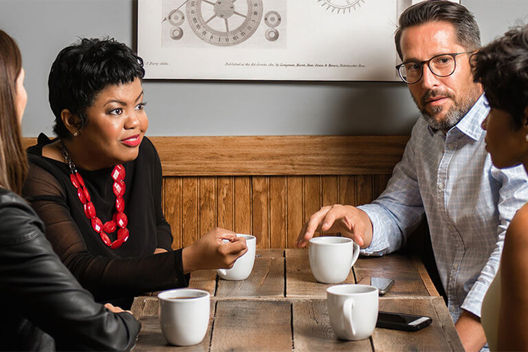 A group of diverse people sitting at a table with coffee cups.